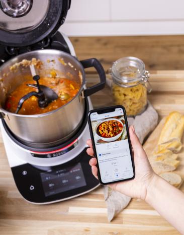 Fertig gekochtes Gulasch im Cookit Topf und ein Smartphone mit App und Cookit Rezept.