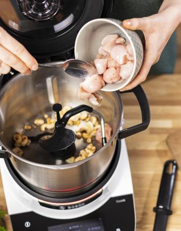 Hähnchenbruststücke werden zu Cashewkernen in den offenen Cookit Kochtopf gegeben Hähnchenbruststücke werden zu Cashewkernen in den offenen Cookit Kochtopf gegeben
