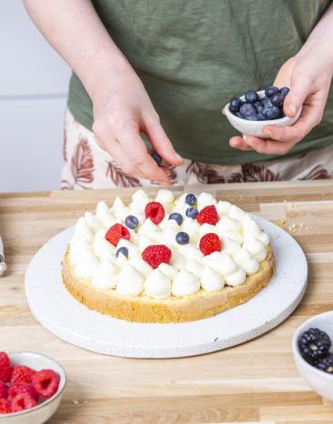 Beeren werden auf Sahnecreme auf Torte verteilt. Beeren werden auf Sahnecreme auf Torte verteilt.