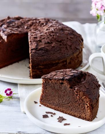 Einfacher Schokokuchen mit einem angeschnittenen Stück auf einer Kaffeetafel.