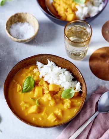 Einfaches Kürbis-Curry mit Reis in einer Schale auf einem gedeckten Tisch mit Kerzen.