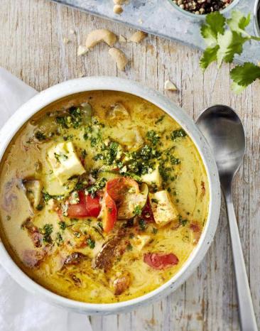 Gemüse-Curry "Jalfrezi" in einer weißen Schale auf einem Holztisch, daneben ein Löffel Gemüse-Curry "Jalfrezi" in einer weißen Schale auf einem Holztisch, daneben ein Löffel
