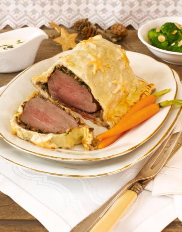 Beef Wellington auf einem gedeckten Tisch, eine Scheibe angeschitten.