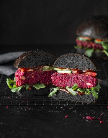 Black Bun Burger mit Rote Bete Patty halb aufgeschnitten auf einer dunkle Platte.