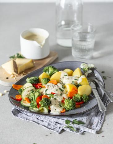 Buntes Gemüse und Kartoffeln in Käsesauce auf einem gedeckten Tisch serviert.