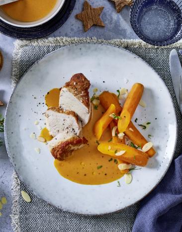 Schweinefilet mit Karotten und Rahmsauce hünsch angerichtet auf einem hellen Teller.
