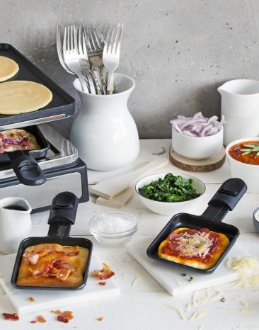 Flammkuchen für Raclette in Pfännchen auf einem gedeckten Tisch.