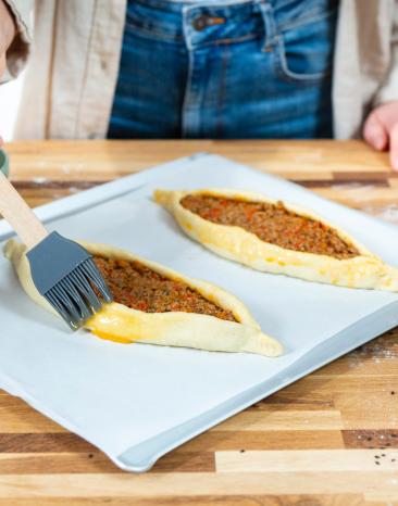 Pide mit Hackfleisch wird mit verquirltem Ei bestrichen. Pide mit Hackfleisch wird mit verquirltem Ei bestrichen.