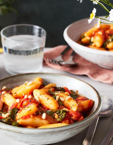 Schupfnudeln mit Spinat und Tomaten serviert auf einem gedeckten Tisch.
