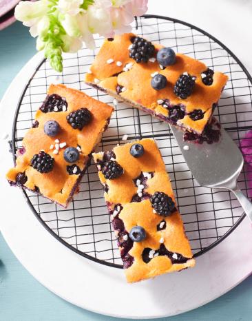 Blechkuchen mit Blaubeeren und Brombeeren in Stücke geschnitten auf einem Kuchengitter.