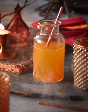 Zauberhafter Kürbissaft in einer Glasflasche mit Stohhalm, dahinter Halloween Deko.