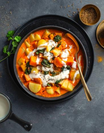 Kartoffelcurry mit Kokosnuss und Kräutern in einer dunklen Schale.