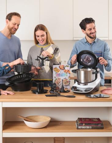 Der Cookit steht mit seinen Tools auf der Küchezeile und fünf Leute betrachten diese. Der Cookit steht mit seinen Tools auf der Küchezeile und fünf Leute betrachten diese.