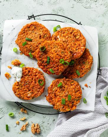 Gemüsepuffer auf einem Gitter, daneben eine Schale mit Kräuterdip