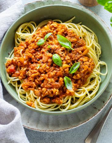 Vegane Bolognese mit Spaghetti in einem hellgrünen tiefen Teller.