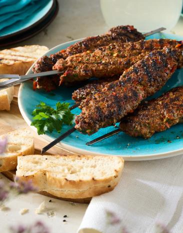 Adana Kebap (Türkische Hackfleischspieße) auf Metallspießen auf einem türkisen Teller.