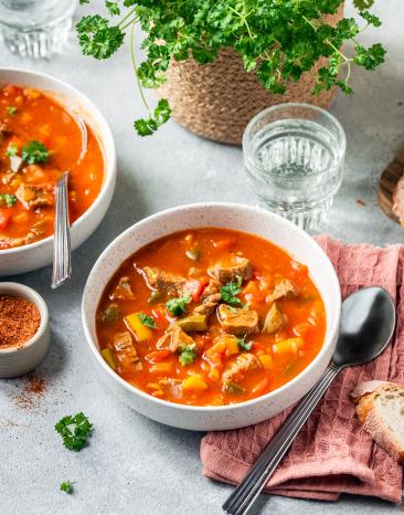 Paprikatopf mediterran mit Rind in Schüsseln auf einem gedeckten Tisch.
