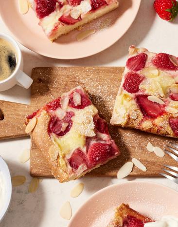 Erdbeerkuchen vom Blech in Stücke geschnitten auf einem Brett.