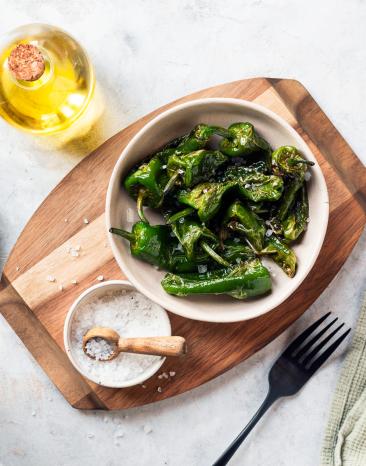 Pimientos de Padron in einer Schüssel auf einem Holzbrett.