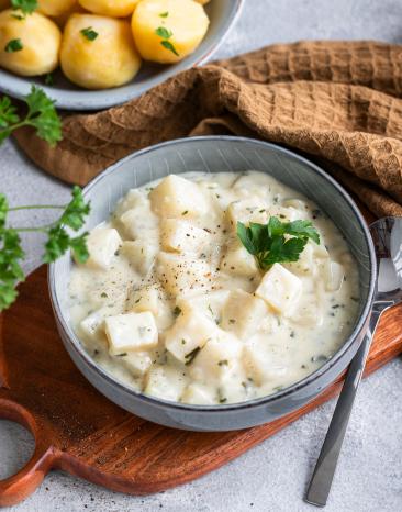 Rahmkohlrabi in einer Schale dazu Kartoffeln und Petersilie.