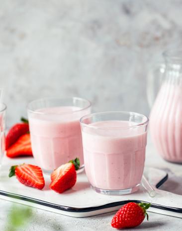 Erdbeer Lassi in Gläsern und einer Glaskaraffe, daneben frische Erdbeeren.
