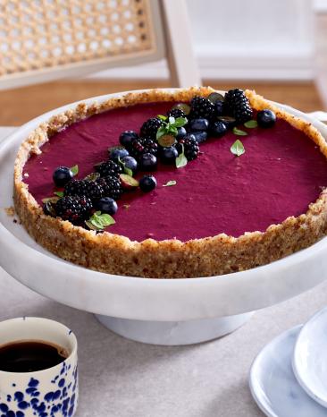 Beerentarte mit lila Beerenfüllung und Beeren als Topping auf einer Tortenplatte.