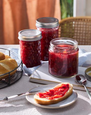 Pflaumenkonfitüre in Einmachgläsern auf einem Tischmit Brot.
