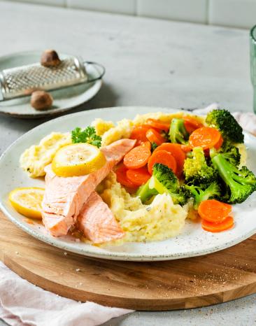 Gedämpfter Lachs mit Gemüse und Kräuterstampf auf einem Teller.