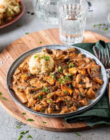 Schwammerlgulasch mit gemischten Pilzen und Klößenauf Tellern.