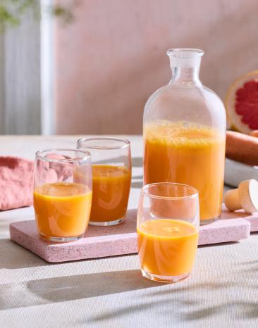 Karotten-Zitrus-Shot in einer Karaffe und Gläsern.