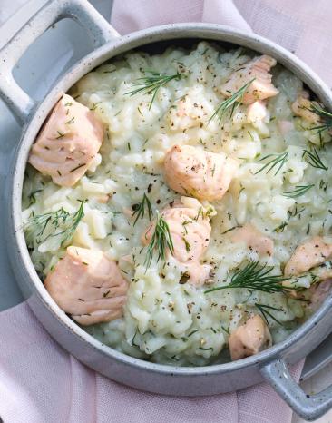 Lachs Risotto in einem hellen Topf mit Fischstücken.