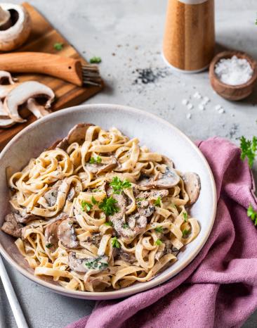 Bandnudeln mit Pilzsauce und Kräutern in einem tiefen Teller, daneben ein Brett mit Pilzen. Bandnudeln mit Pilzsauce und Kräutern in einem tiefen Teller, daneben ein Brett mit Pilzen.