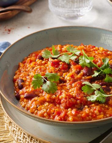 Chili sin carne mit Graupen und frischen Kräutern in einer Schüssel.