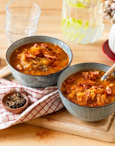 Sauerkrautsuppe mit Speck in Schüsseln mit rustikalem Tuch.