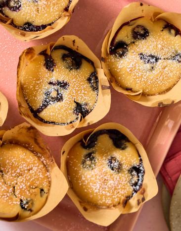 Vegane Blaubeer-Muffins in Papierförmchen auf einem Tablett.