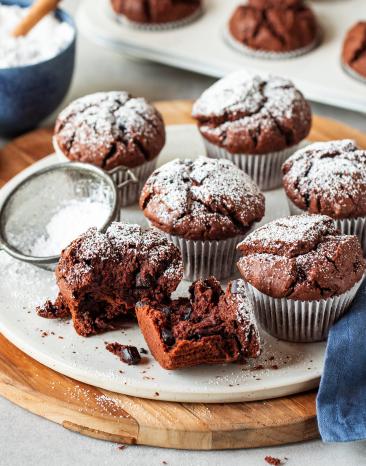 Saftige Schokomuffins in Papierförmchen mit Puderzucker bestäubt.