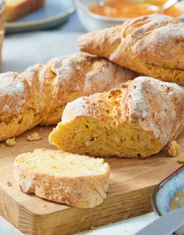 Baguette auf einem Holzbrett, angeschnitten, auf einem Frühstückstisch.