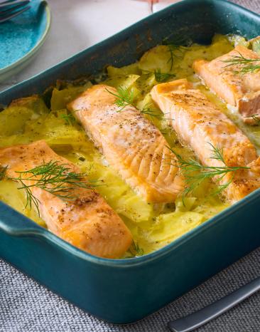 Kartoffel-Zucchini-Auflauf mit Lachs in einer blauen Auflaufform auf einem Tisch.