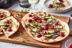 Flammkuchen belegt mit Himbeeren, Zucchini und Ziegenkäse auf einem Holzbrett.